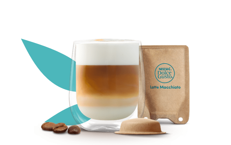tasse avec un Latte Macchiato à côté d'une capsule et d'un sachet à base de papier