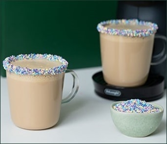 Deux tasses de café crémeux dont les bords sont décorés de paillettes colorées et un petit bol de paillettes