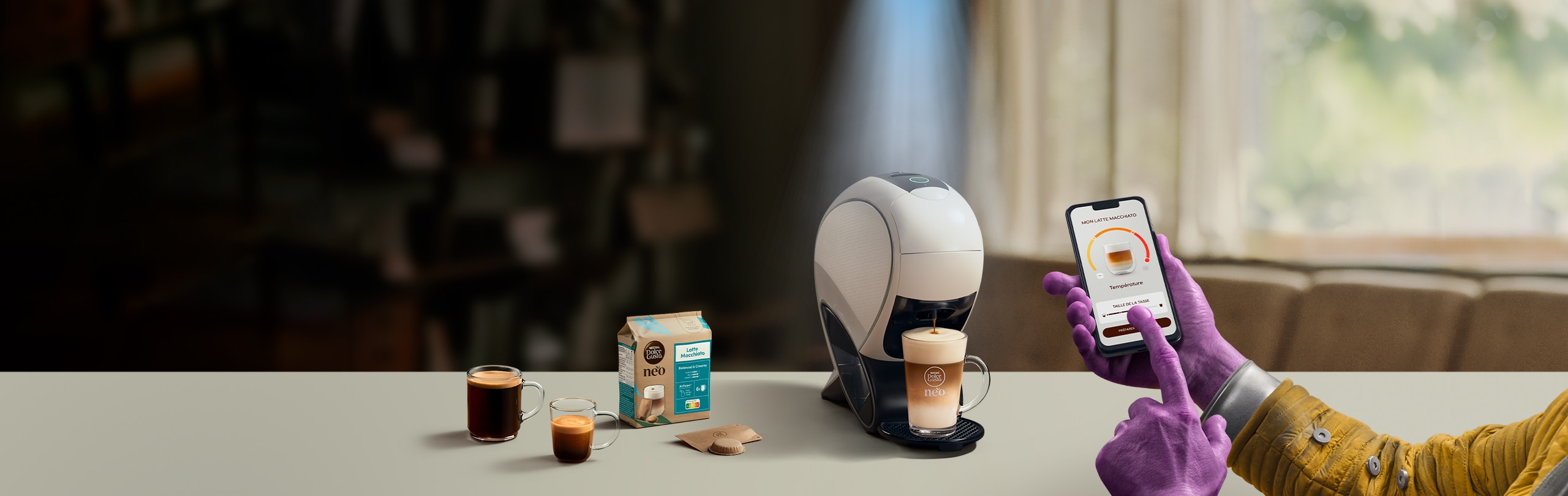 Une main d'alien utilisant l'application NESCAFÉ Dolce Gusto pour personnaliser un café. Machine à café intelligente NEO Latte, pack de café et boissons.