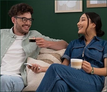 Un couple souriant assis sur leur canapé, profitant ensemble des cafés NESCAFÉ Dolce Gusto